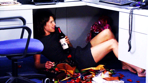 A person clutches wine bottle under cubicle desk