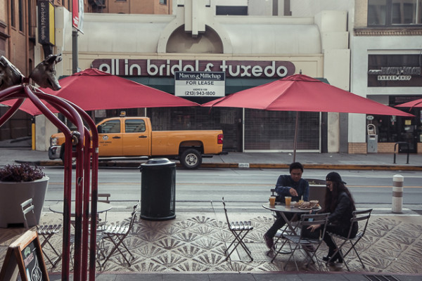 Like New York before it, Los Angeles has developed a strong culture of "sidewalk cafes," built for quick eating while commuting by foot. Here, two pedestrians spend a few minutes eating food from the Grand Central Market before going on their way.