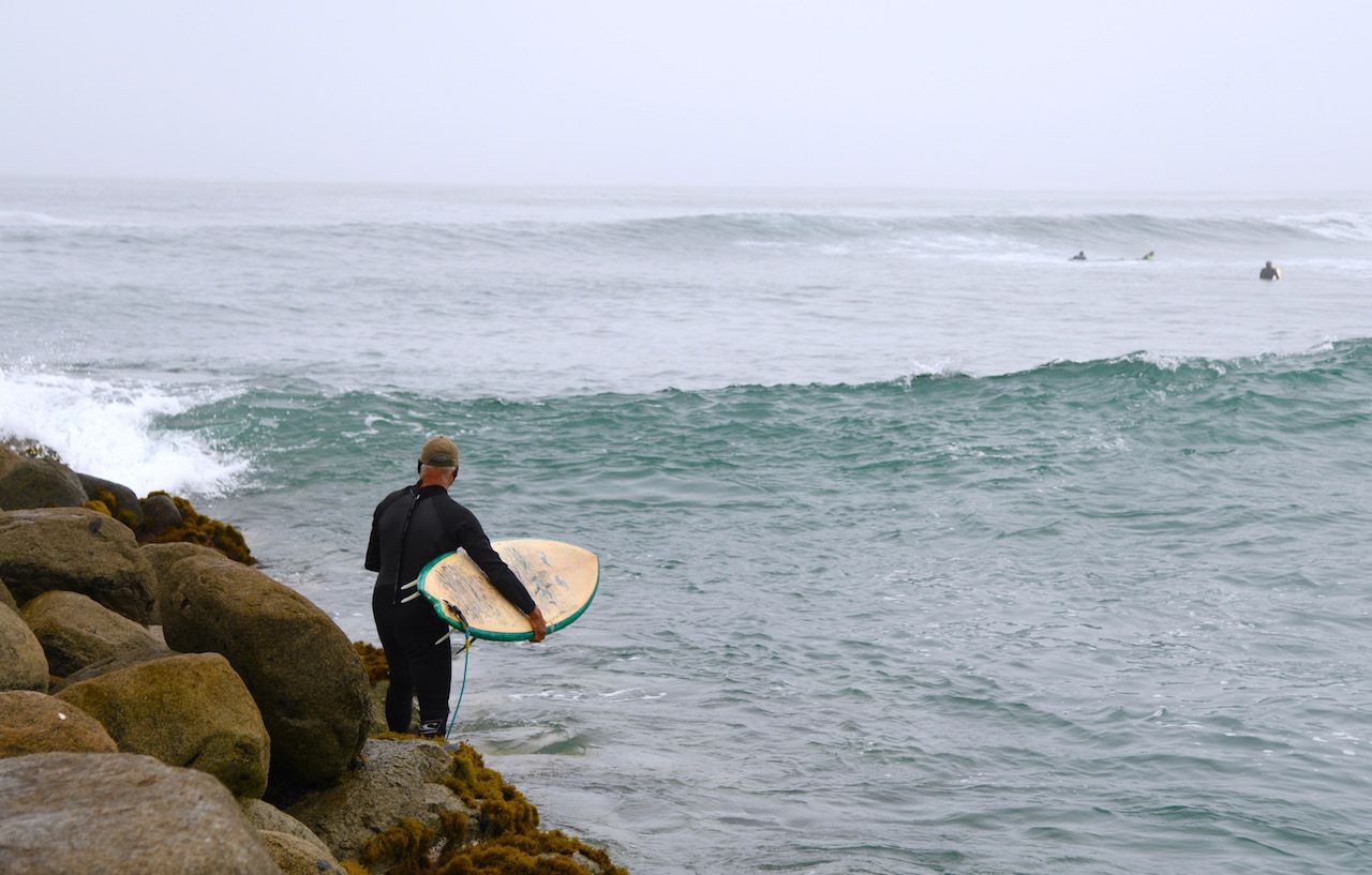 Old surfer getting in water at San Bartolo Peru