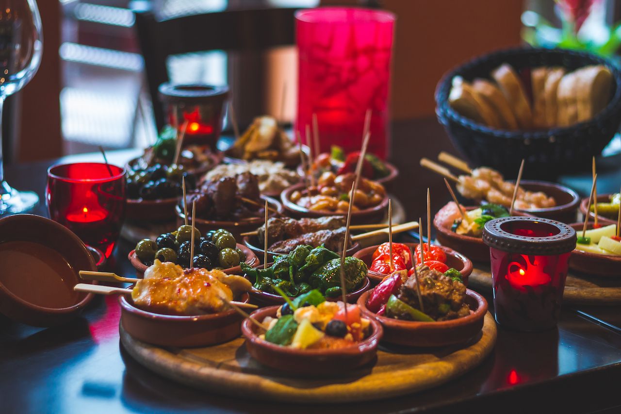 a wide selection of Spanish tapas with toothpicks on a table with candles
