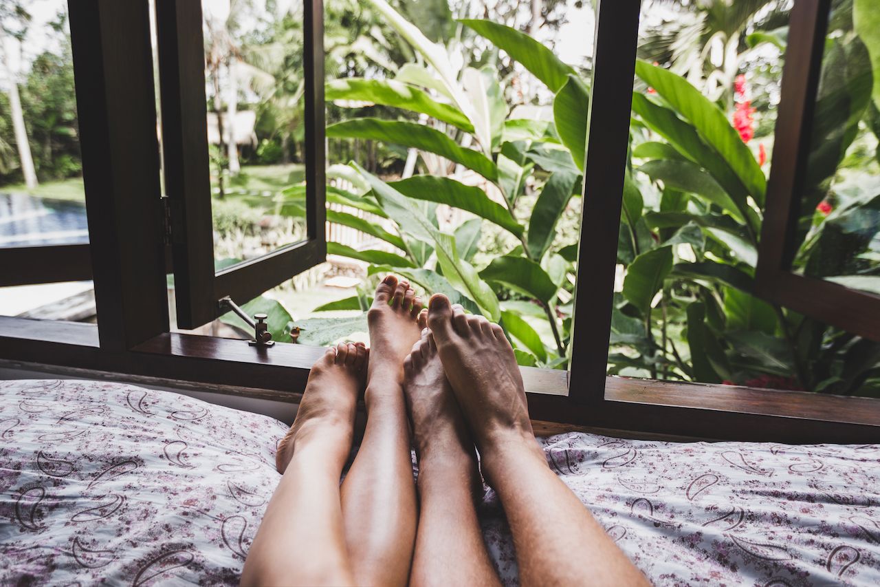 Legs of couple in love in bed in the morning, view from window on tropical garden