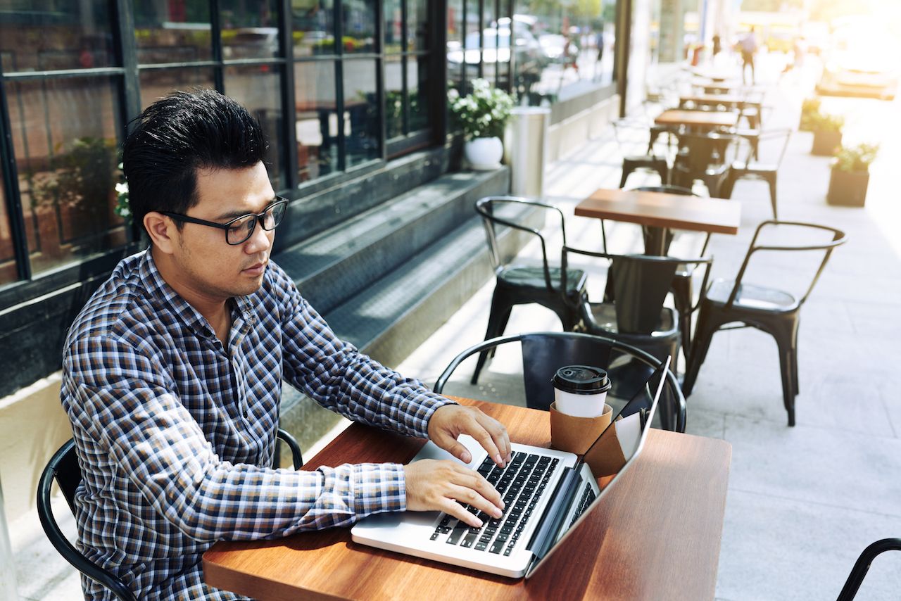 Young Vietnamese businessman working on laptop in outdoor cafe