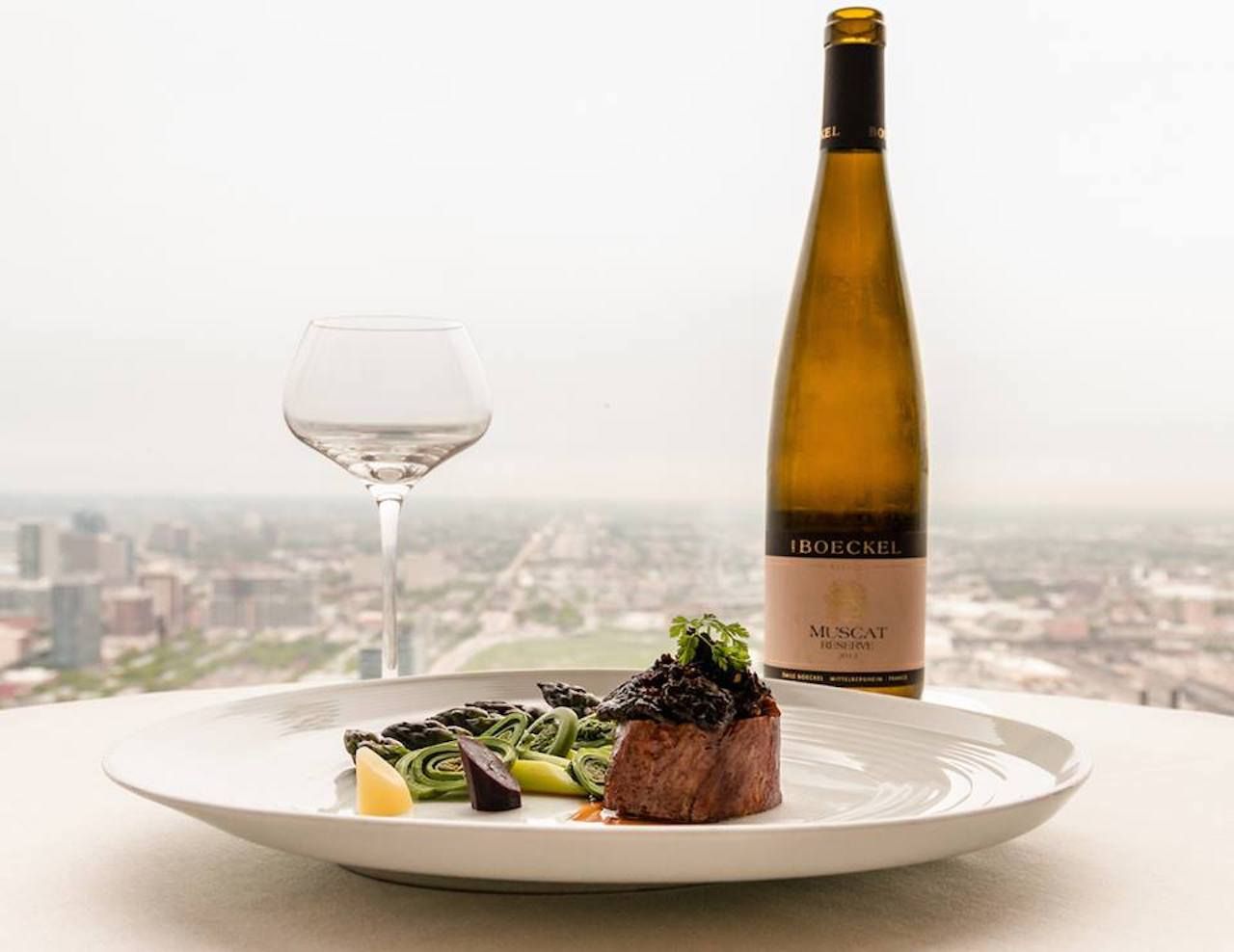 Bottle of wine and steak dish in front of restaurant window with view of Chicago