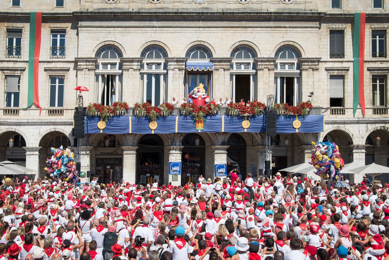 Crowd of people dressed in white and red cheering King Leon on the balcony at the Summer Festival of Bayonne