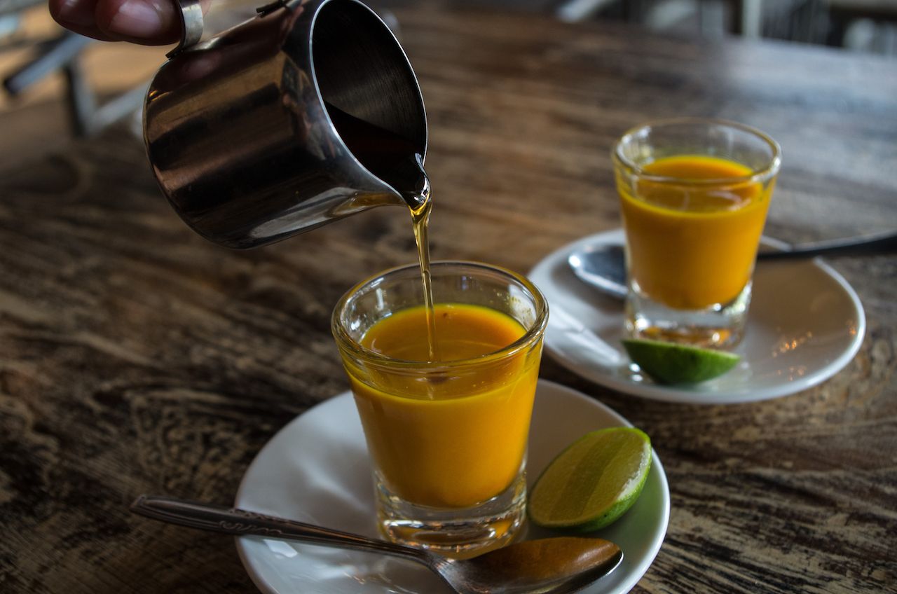 Adding honey to two healthy jamu shots in close-up