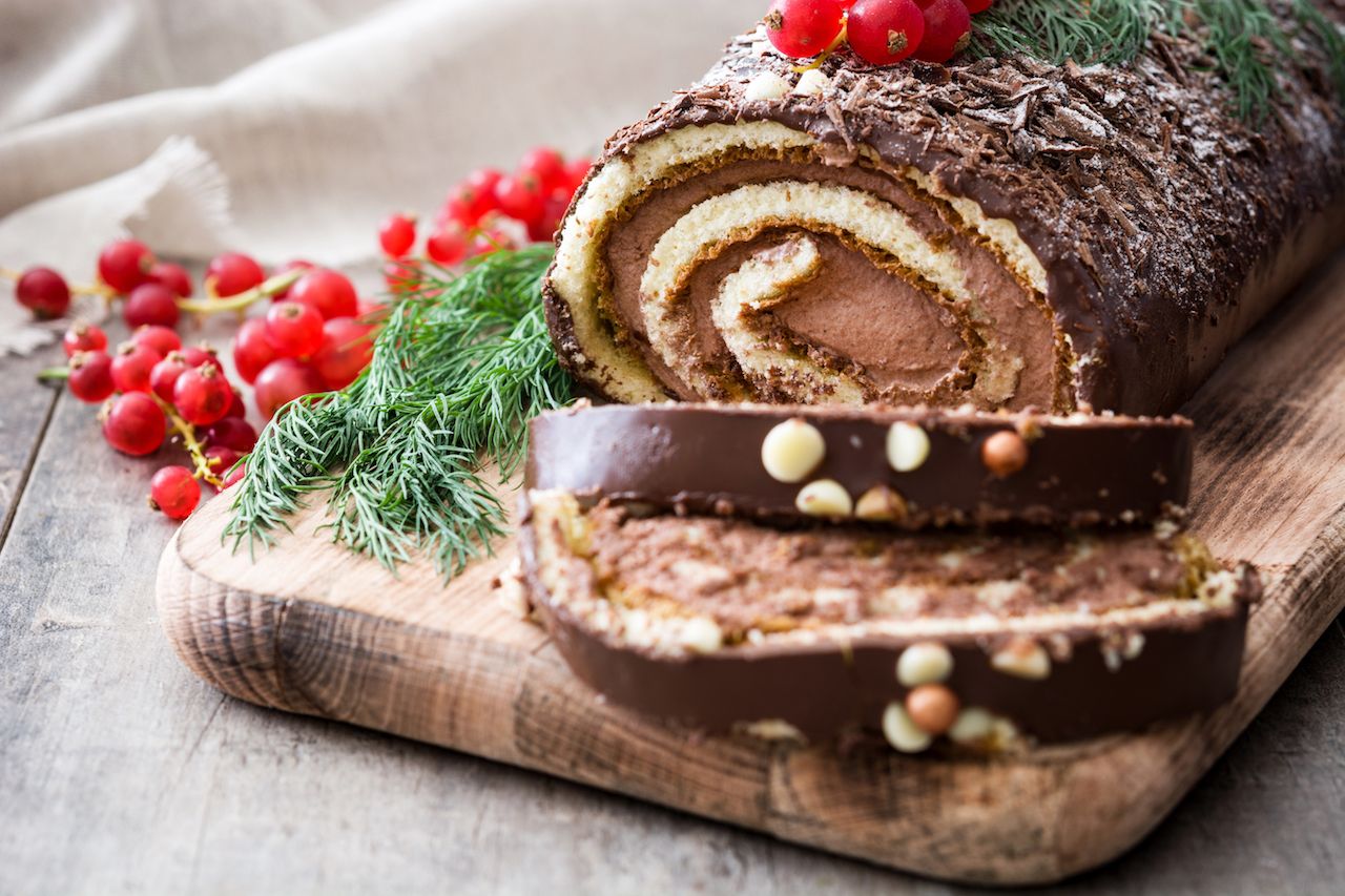 Chocolate yule log christmas cake with red currant on wooden background