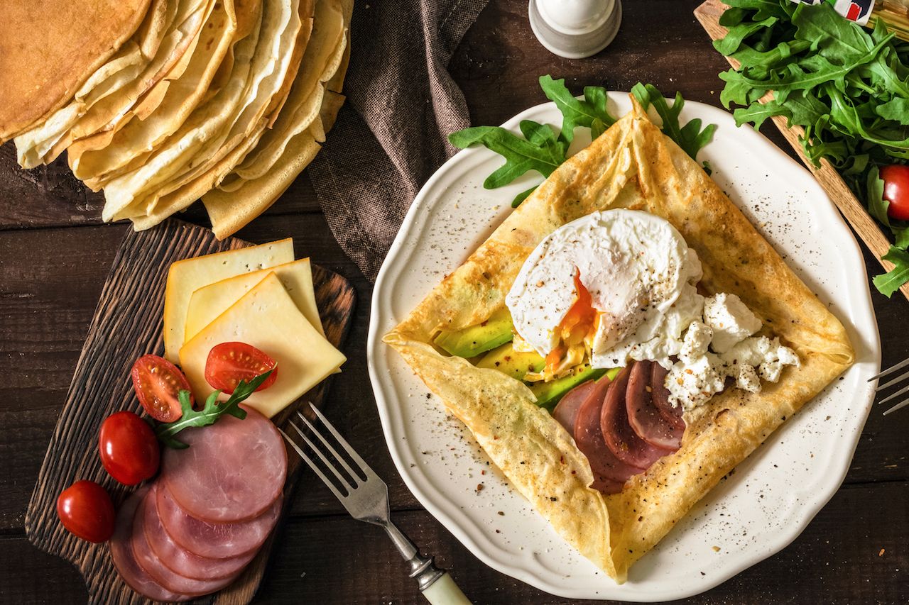 Crepe pancake with ham, avocado, soft white cheese and egg on white plate