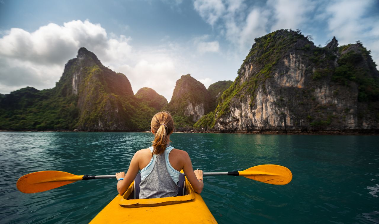 Woman exploring calm tropical bay with limestone mountains by kayak