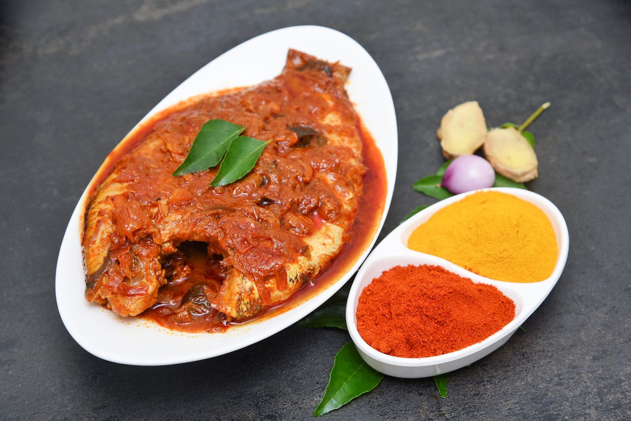 Bengali fish curry next to vibrant red and yellow spices
