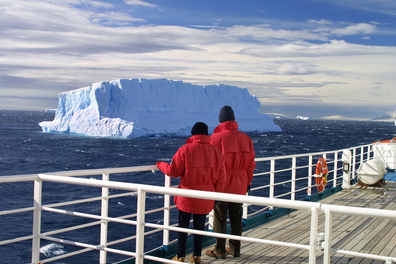 Cruise ship passengers looking at a beautiful iceberg at Antarctica