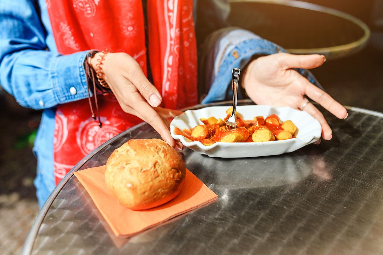 Person eating Currywurst with bread in Berlin street food cafe