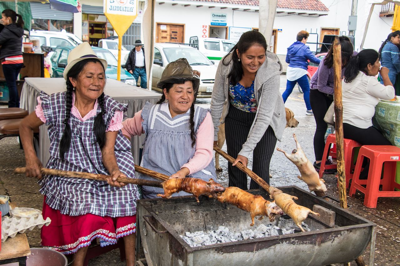 Peruvian women roasting guinea pigs on a spit
