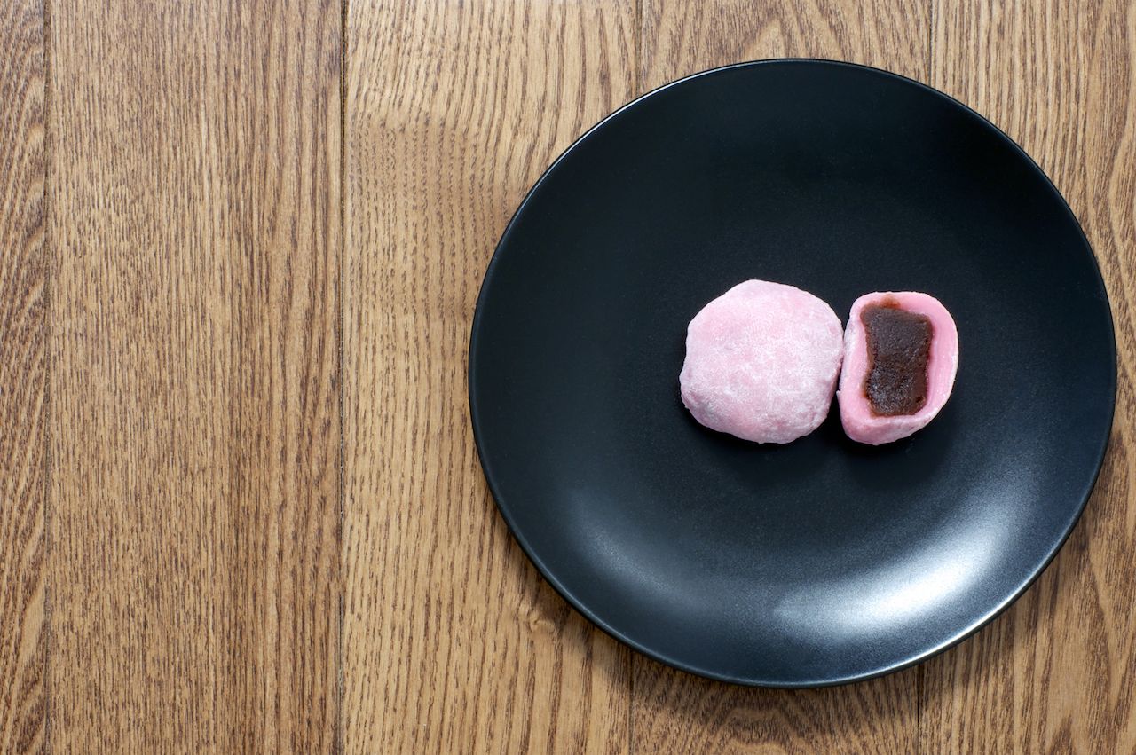 Pink mochi japanese cut sweet rice treat with filling on the black plate