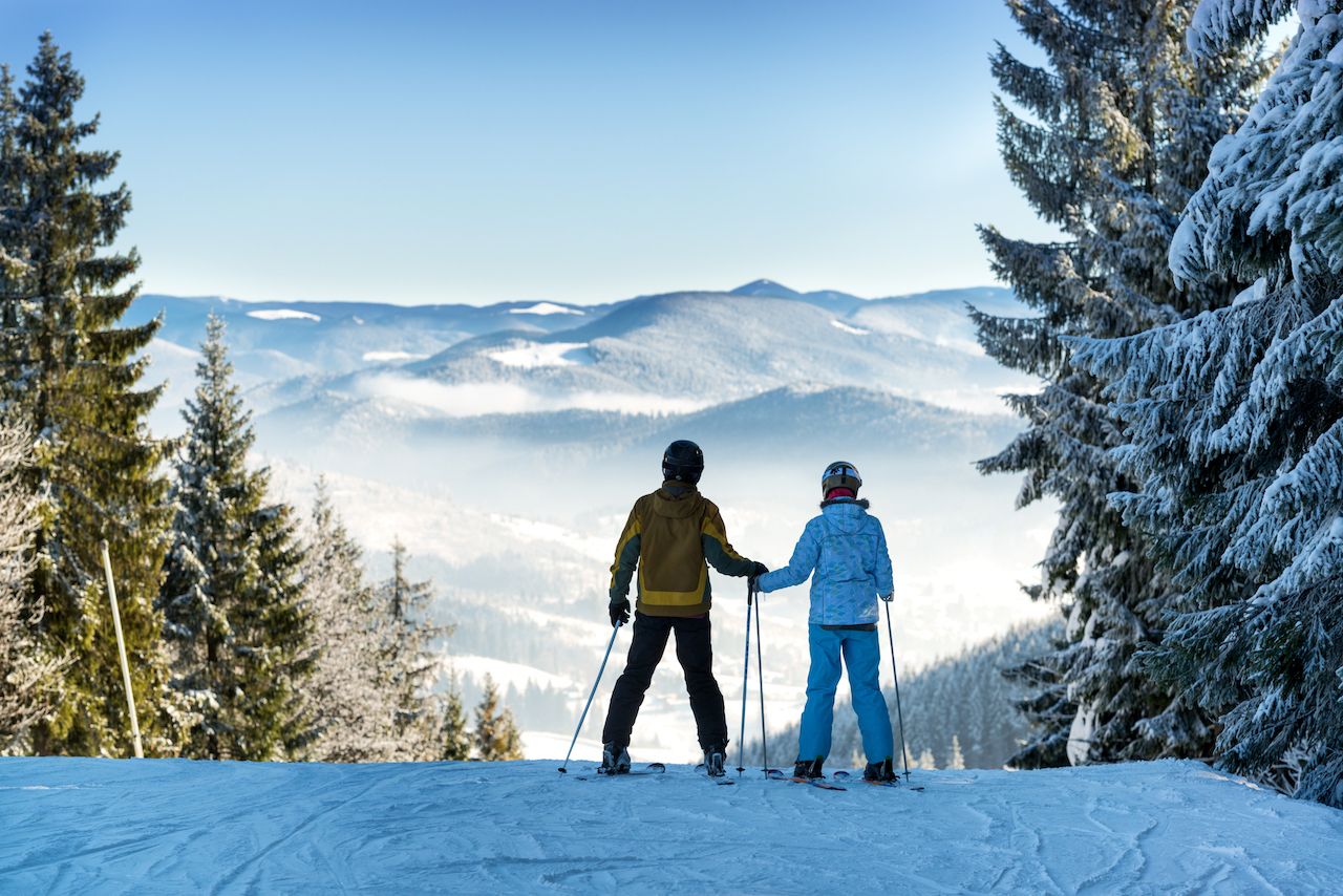 Man and woman skiers keeping hands and enjoying beautiful mountain landscape on a winter resort
