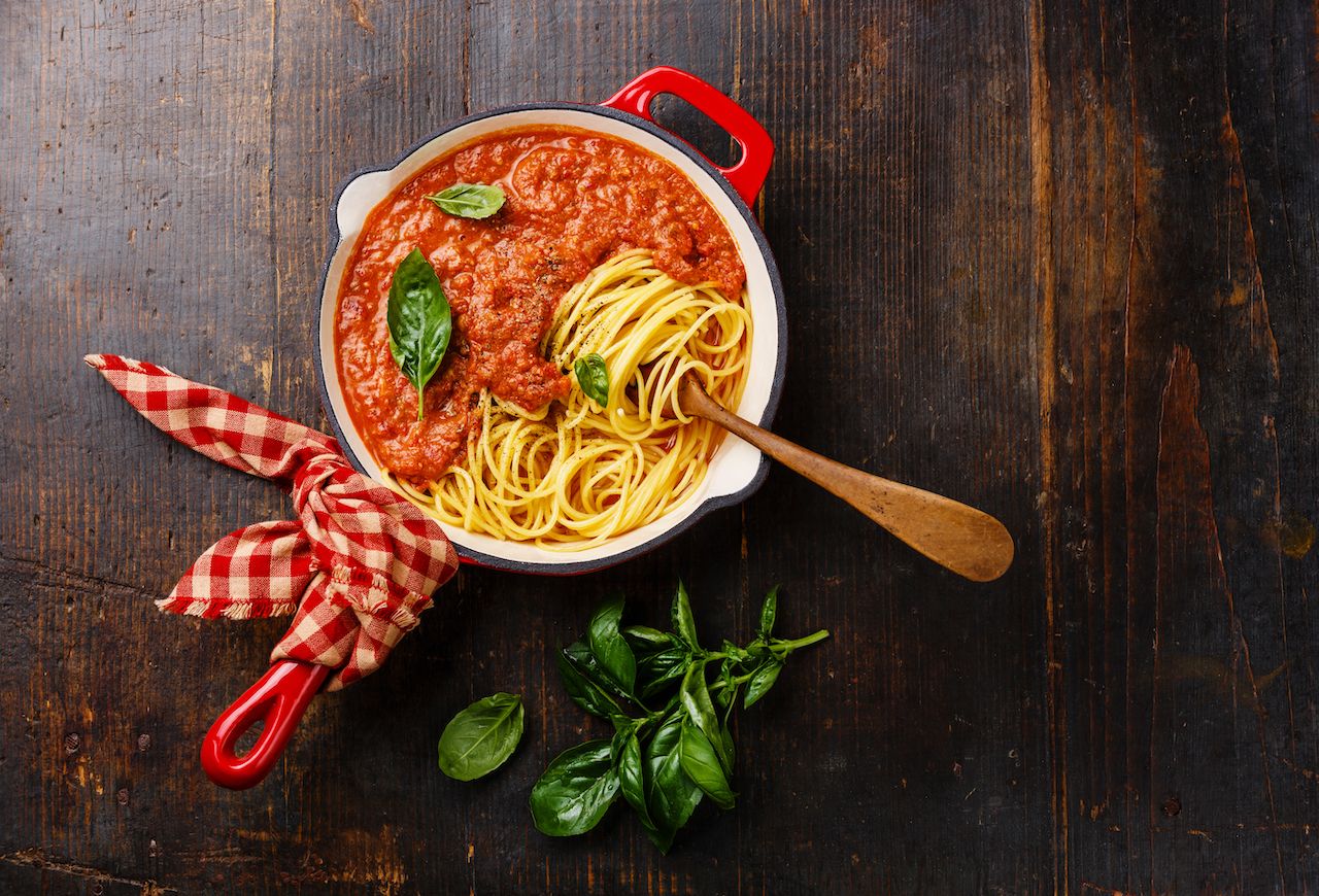 Spaghetti Bolognese with tomato sauce and basil in iron pan on wooden background