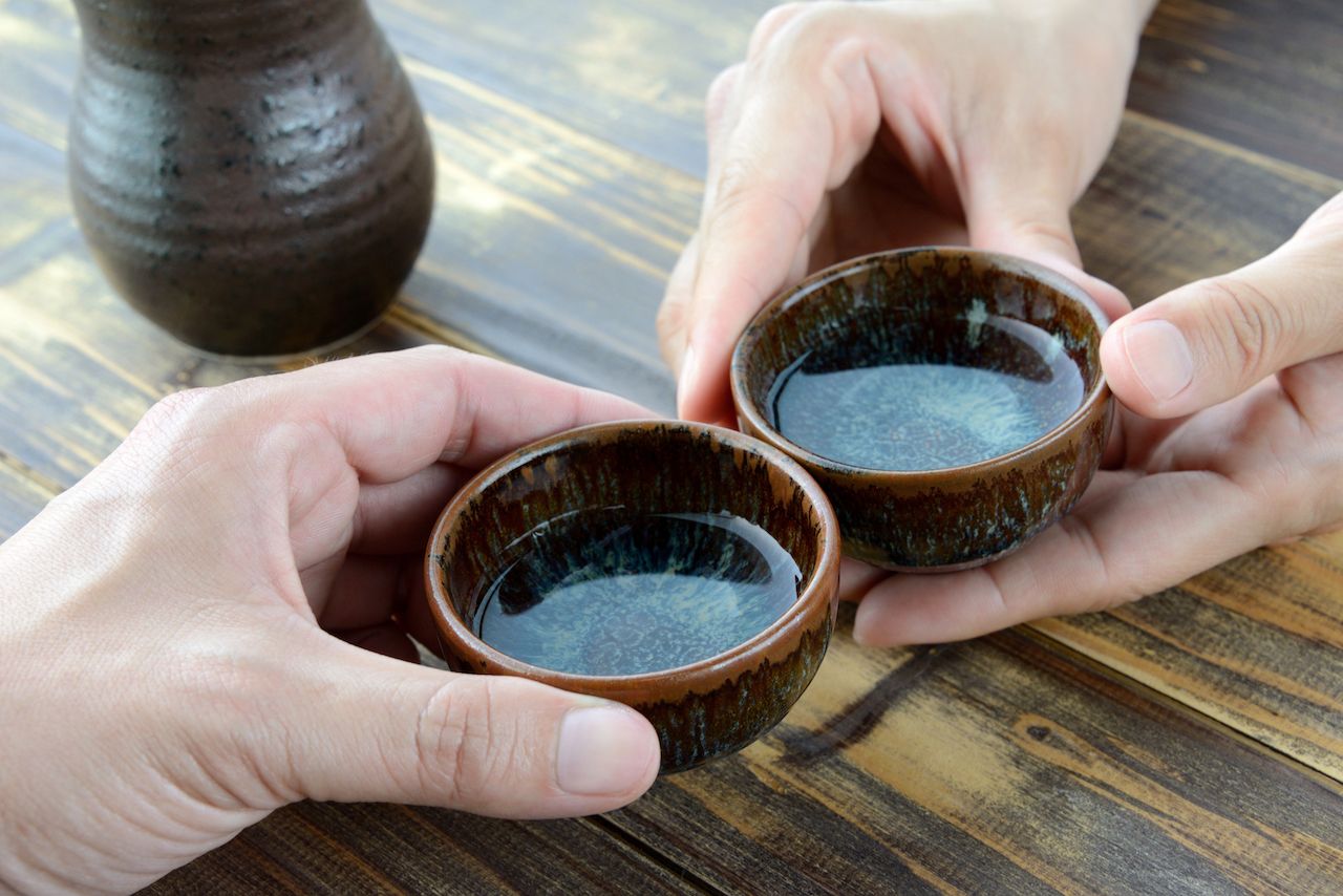 close up on two people holding small brown cups filled with Japanese sake