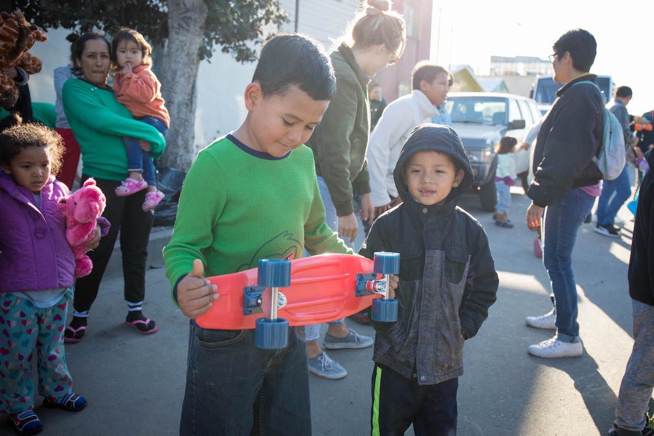 Migrant kids holding a skateboard with onlookers