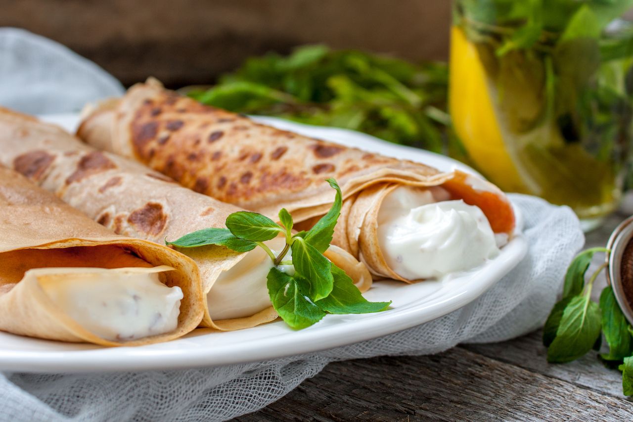 Russian thin pancakes with cheese, butter, jam, mint on a wooden background