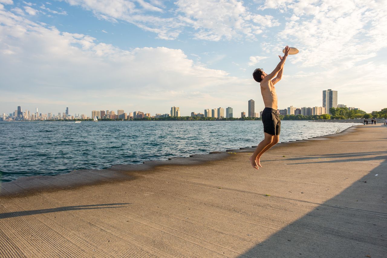 A young man jumps to catch a frisbee in midair in the park area at Montrose Beach