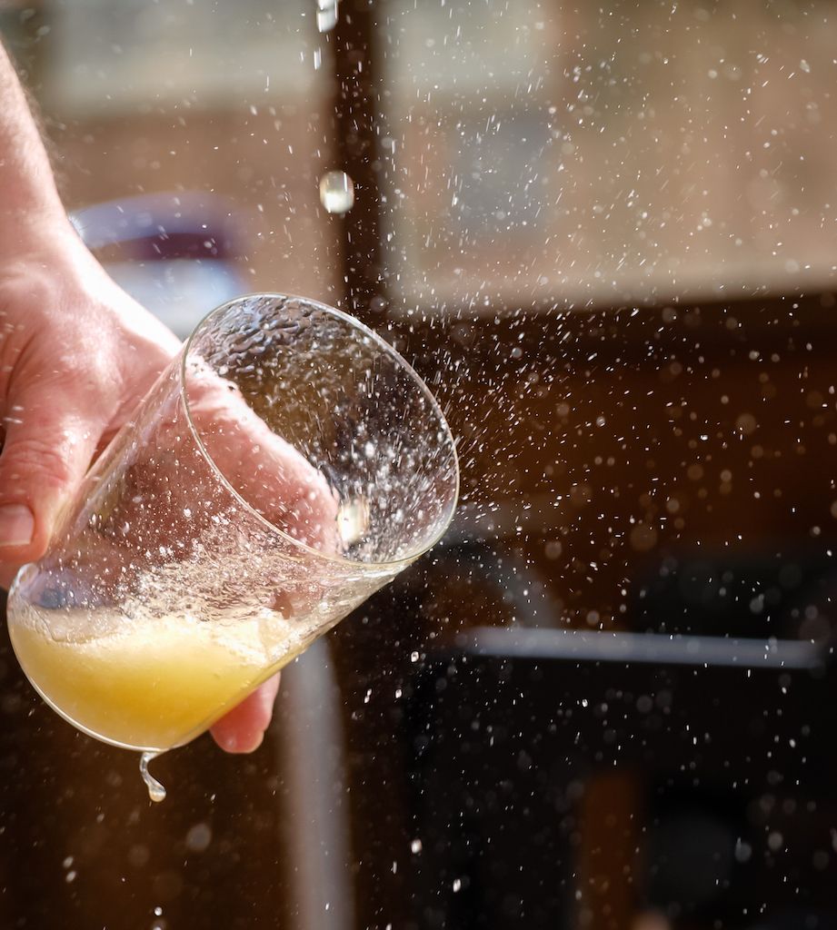 Man hand holding a glass with apple cider splashing outside and drops