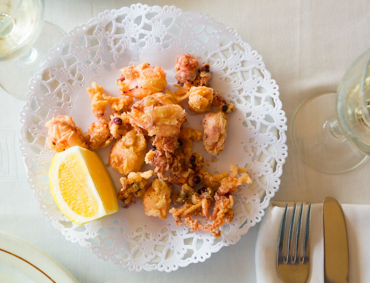 Chipirones, battered fried baby squid served with lemon on white plate