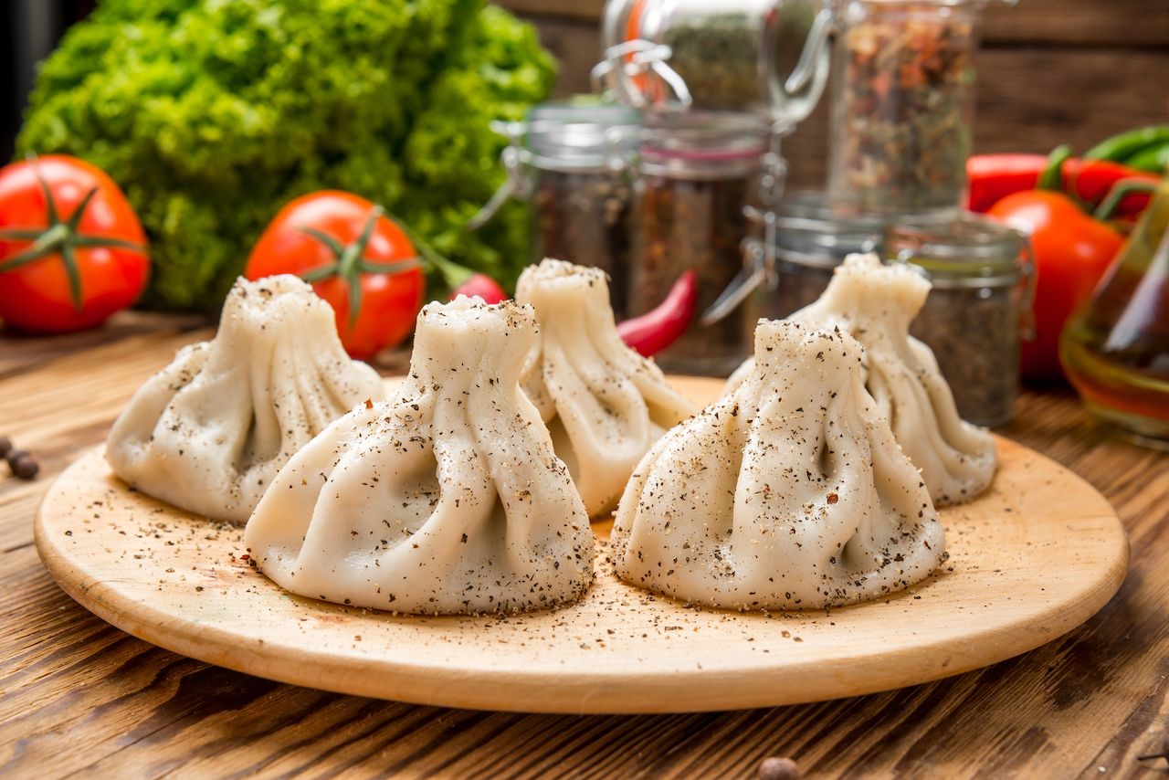 Georgian Khinkali dumplings with meat, greens and tomato spicy Satsebeli sauce on white plate