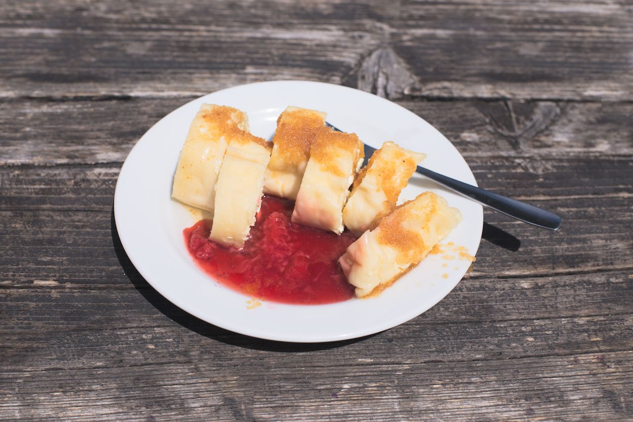 Traditional Slovene Struklji with strawberry jam on a white plate, wood as background