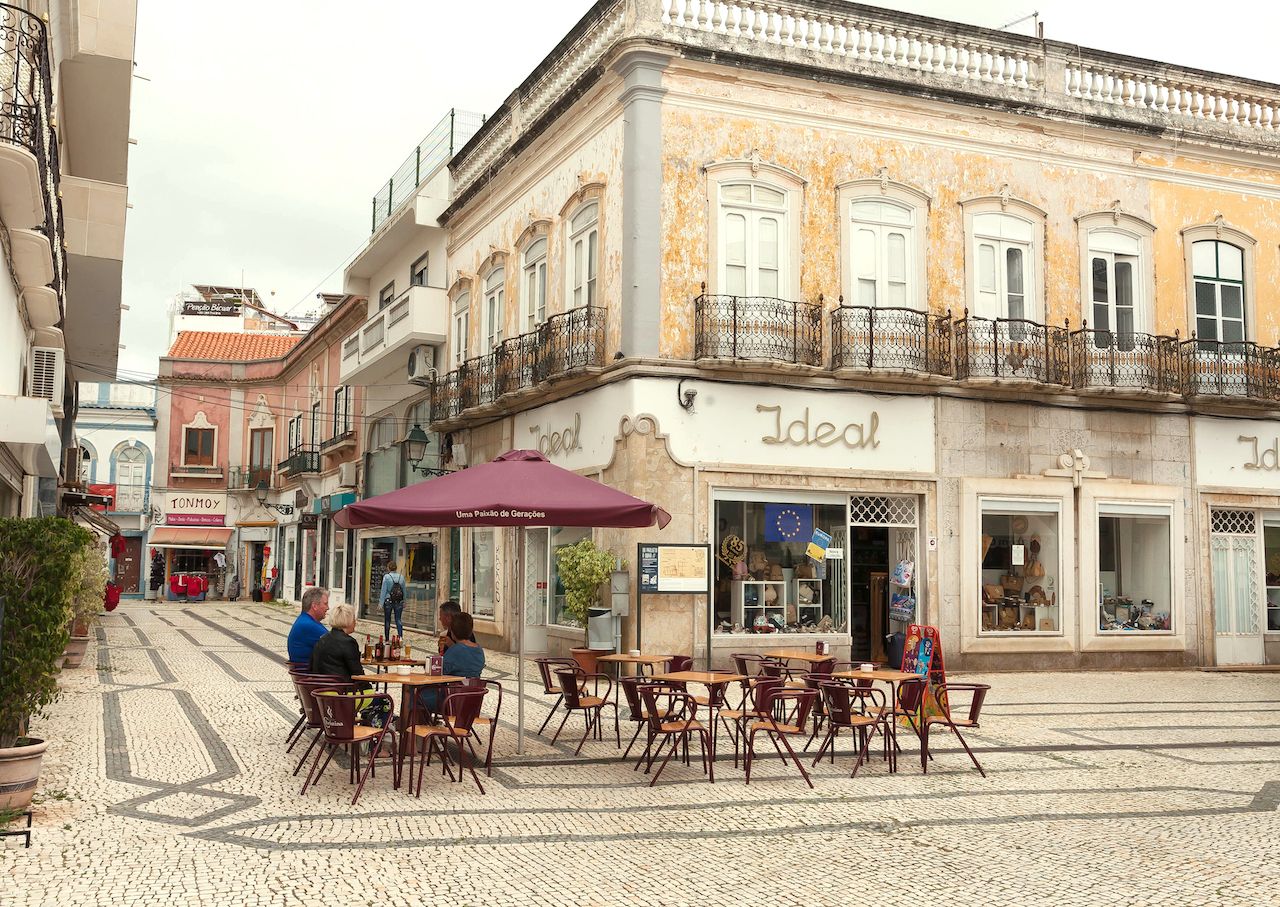 People drinking at outdoor cafe on historical street of Algarve