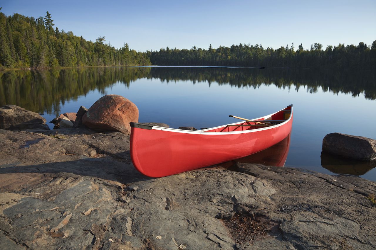 A red canoe rests on a rocky shore of a calm blue lake in the Boundary Waters of Minnesota