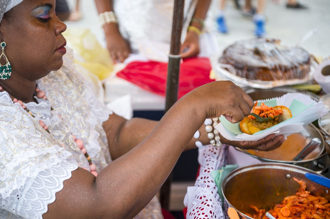 Brazilian Baiana woman assembles a plate of traditional acaraje fritters from a stall on the street.